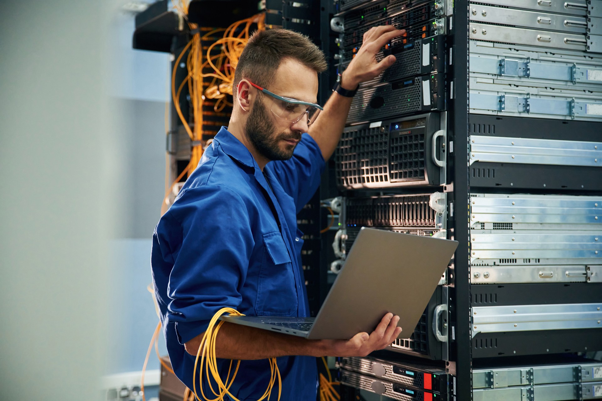 Using the laptop. Young man is working with internet equipment and wires in server room